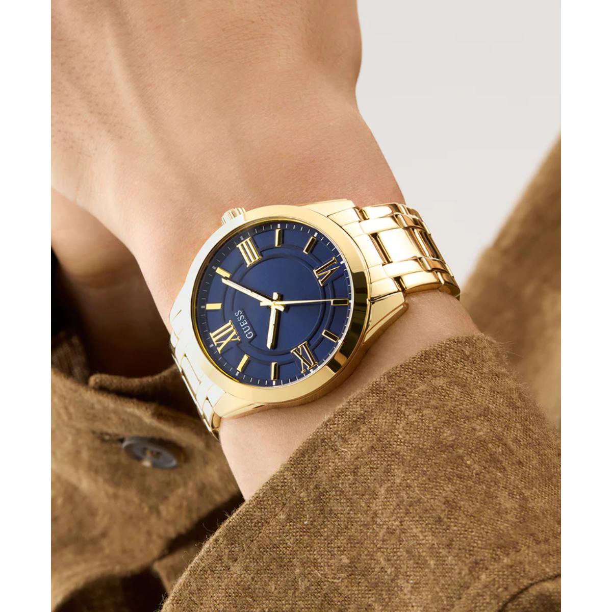 Gold wristwatch with a blue dial on a person's wrist, wearing a brown coat.
