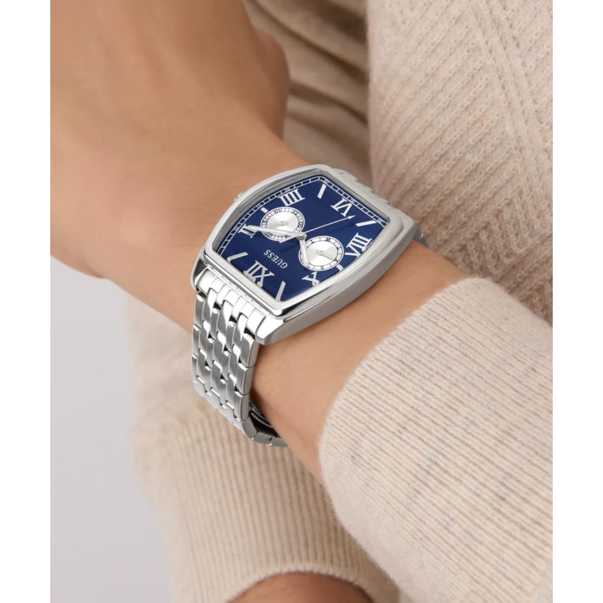 Silver watch with a blue face on a wrist, wearing a beige sweater.