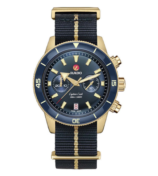 A Rado Captain Cook Chronograph watch with a blue dial, gold-colored casing, and a navy fabric strap with a gold-colored stripe.