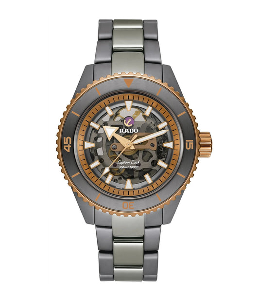 A Rado Captain Cook High-Tech Ceramic Skeleton watch with a rose-gold-colored index ring, a gray monobloc case, and a matching bracelet. The watch has a clear skeleton dial showcasing the movement.
