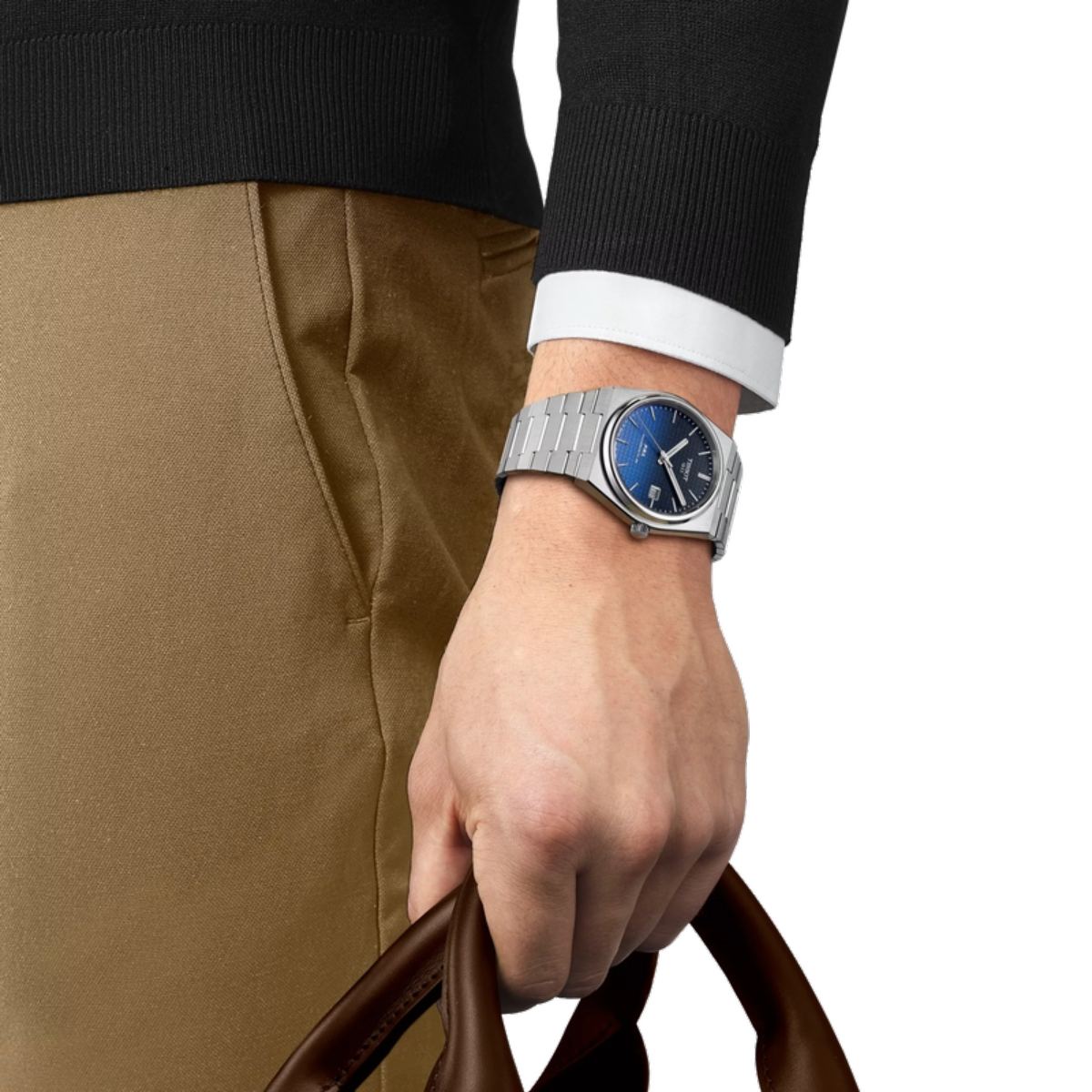 Hand wearing a silver watch with a blue face, holding a brown leather bag on a white background.