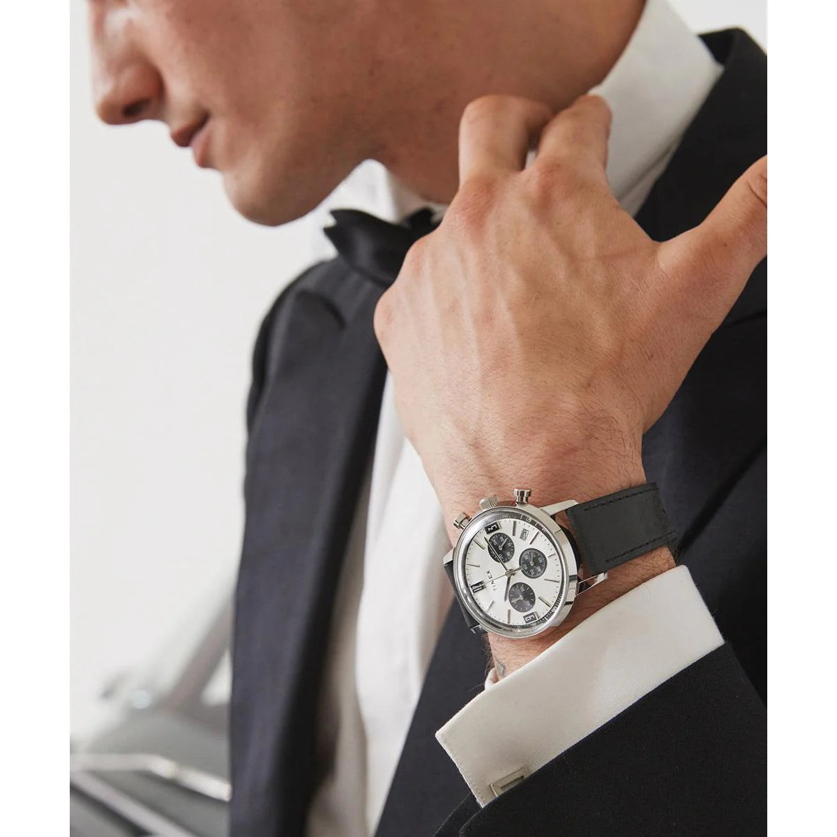 Man wearing a black watch with a white dial in a formal setting