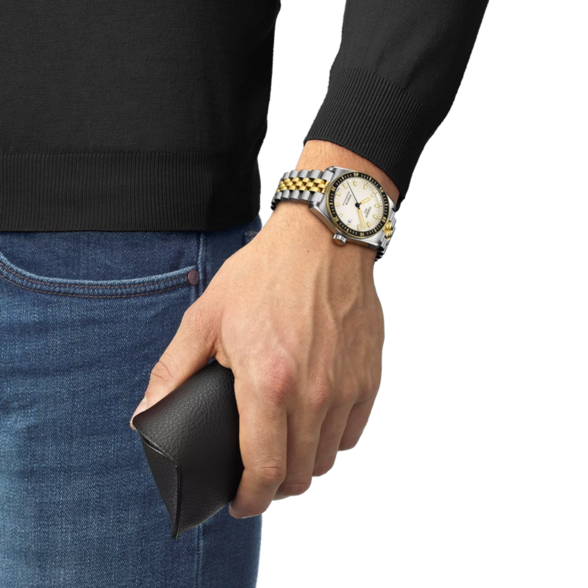 Hand wearing a watch with a black leather wallet, black sweater, and blue jeans on a white background