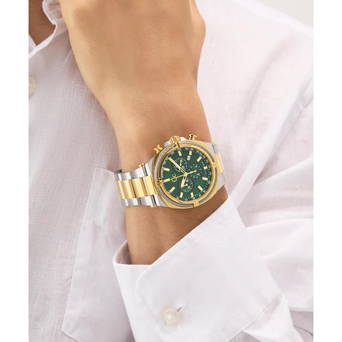 Gold and silver watch with green face on a wrist, wearing a white shirt.
