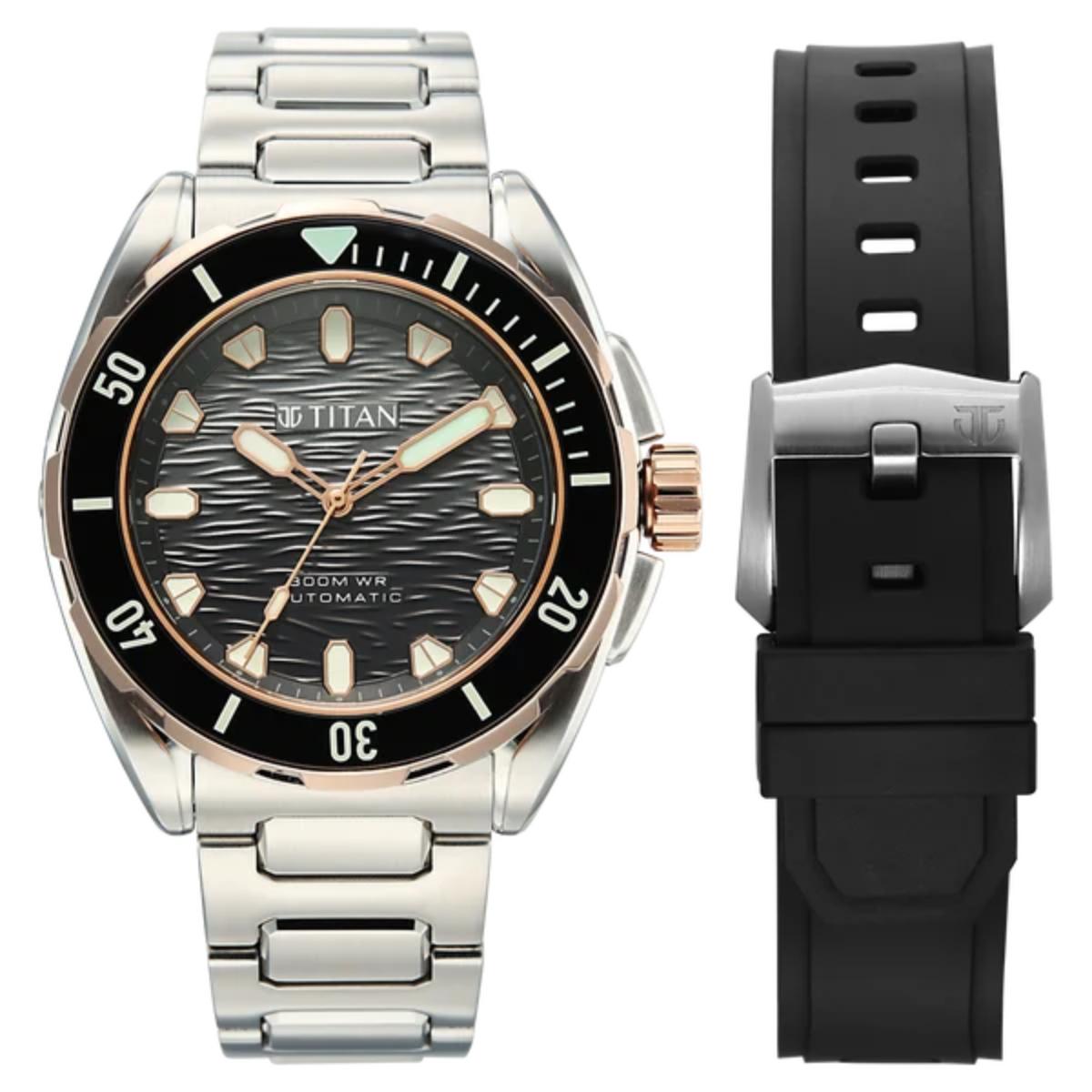 Titan automatic watch with a stainless steel link bracelet, black bezel, and black dial, shown alongside a separate black silicone strap with a silver buckle on a white background.