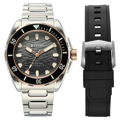 Titan automatic watch with a stainless steel link bracelet, black bezel, and black dial, shown alongside a separate black silicone strap with a silver buckle on a white background.