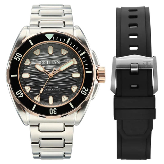 Titan automatic watch with a stainless steel link bracelet, black bezel, and black dial, shown alongside a separate black silicone strap with a silver buckle on a white background.