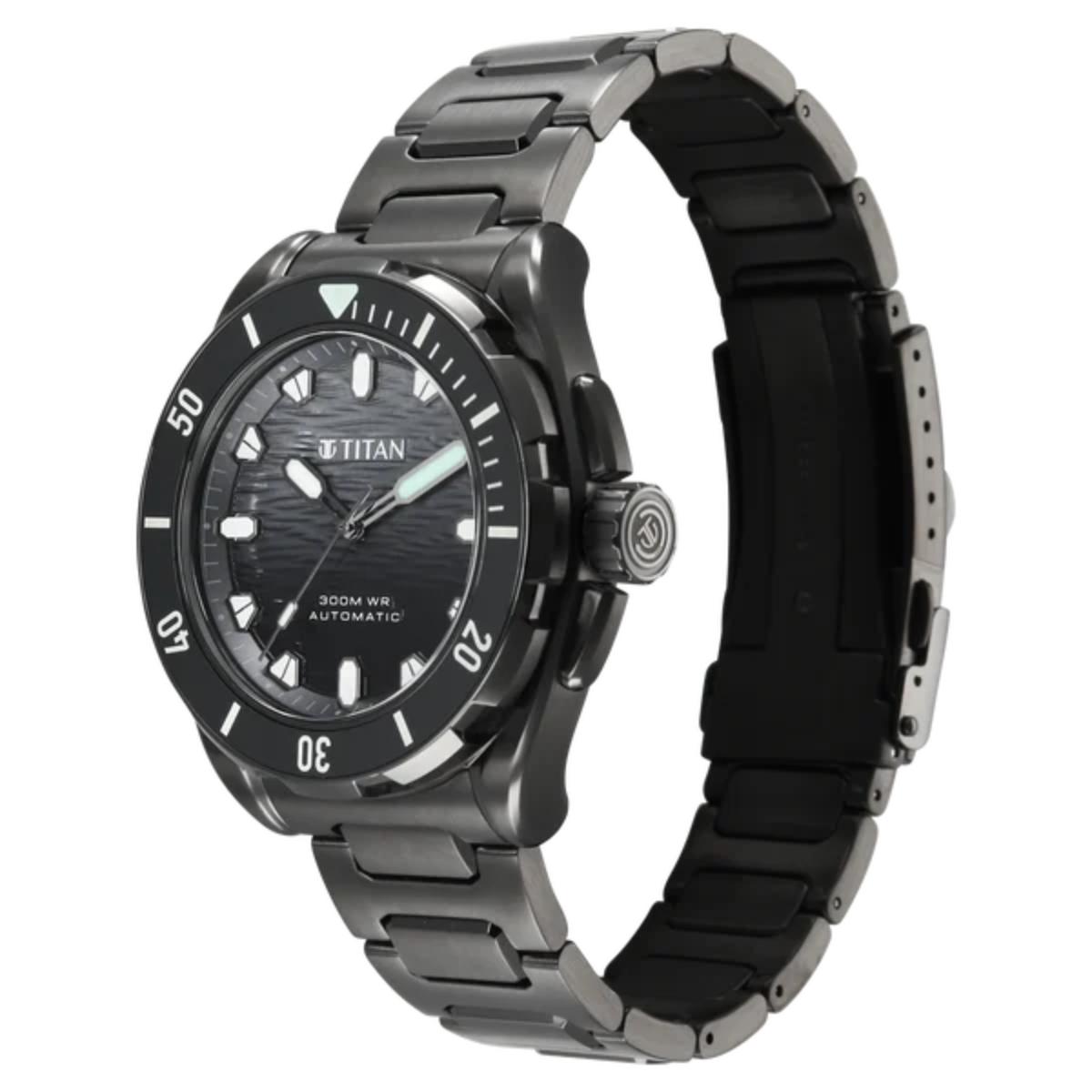 A titanium analog watch with a dark gray and black metal link bracelet, a black textured dial, and a black bezel with white hour markers.