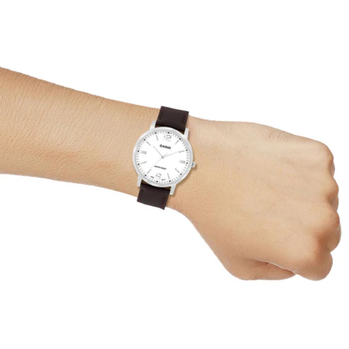 Wrist wearing a watch with a white face and brown strap on a white background