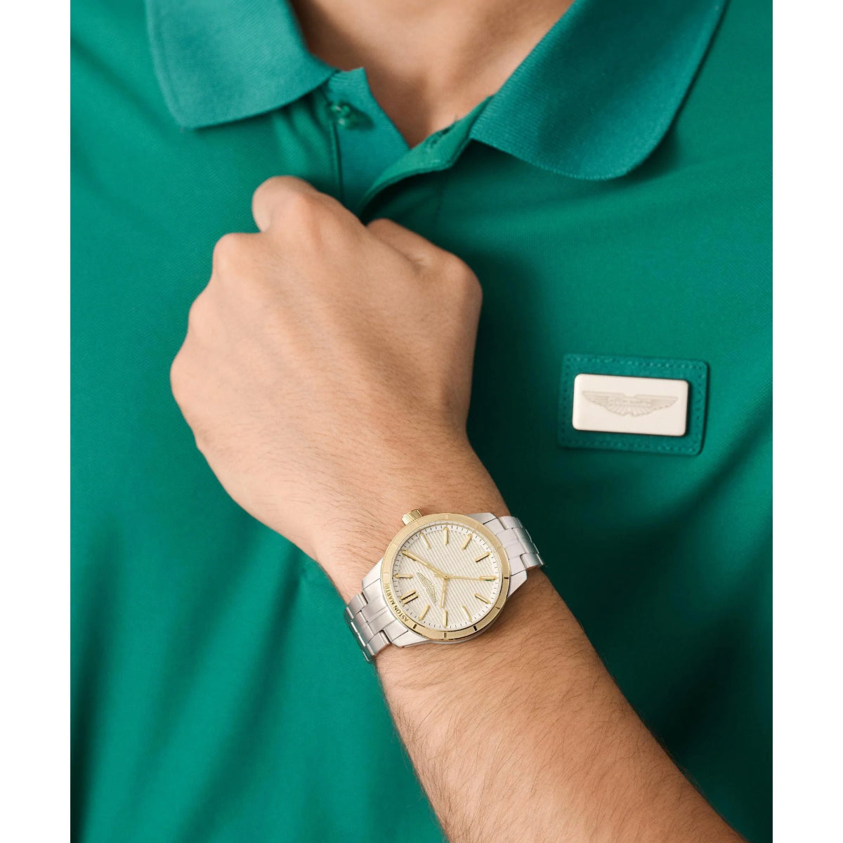 Person wearing a green polo shirt with a logo and a gold watch on a white background