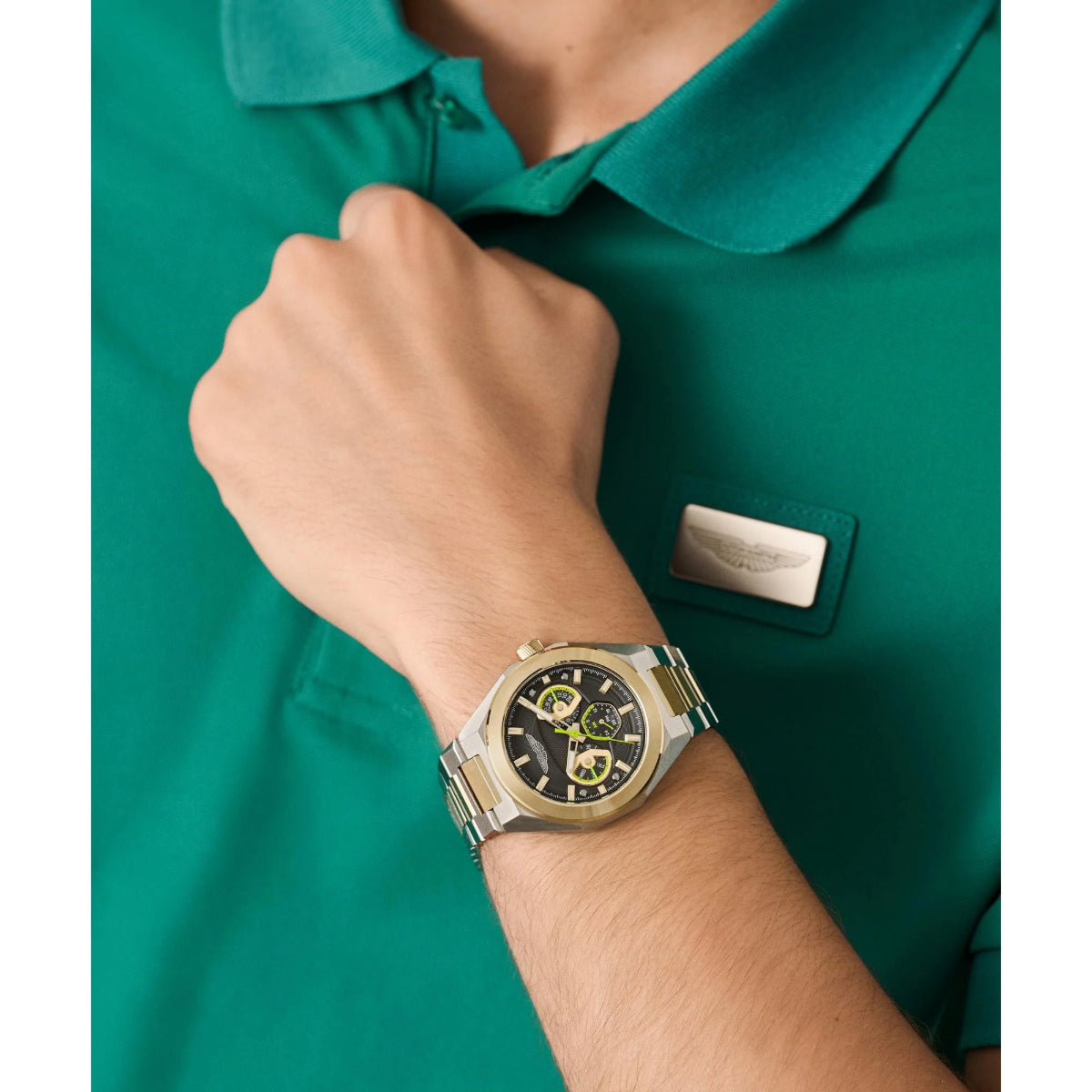 Person wearing a gold watch on a green shirt background