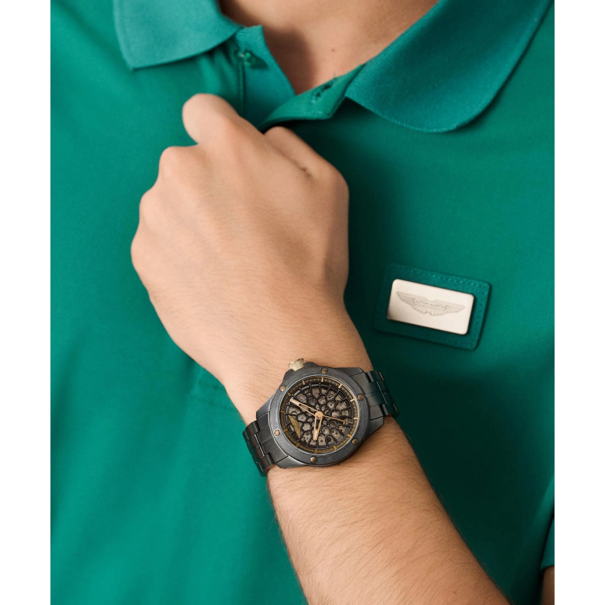Person wearing a green polo shirt with a logo and a black watch on a white background