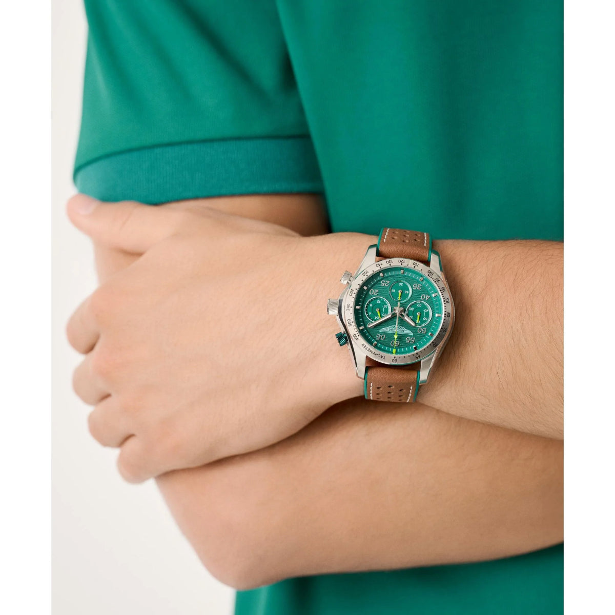 Person wearing a watch with a green face and brown strap on a white background
