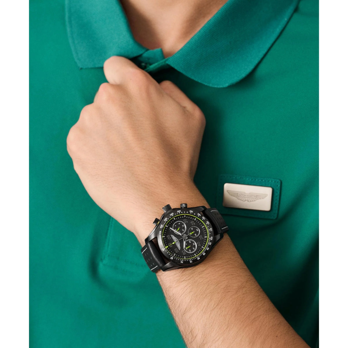 Person wearing a black watch on a green shirt with a visible brand logo.