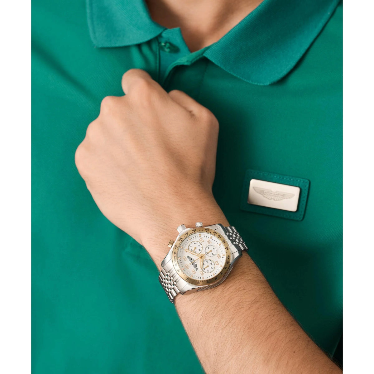 Person wearing a silver watch on a green polo shirt with a logo.