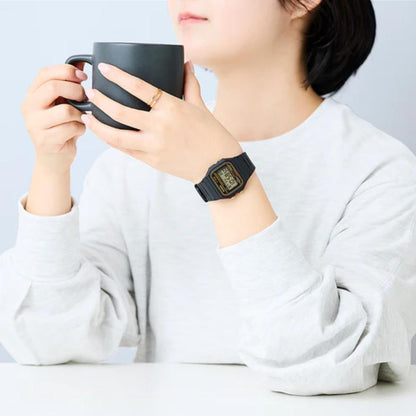 Person holding a black mug with a watch on wrist, wearing a white shirt against a light gray background