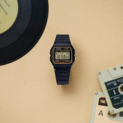 Black Casio digital watch on a beige surface with a record and tape player in the background