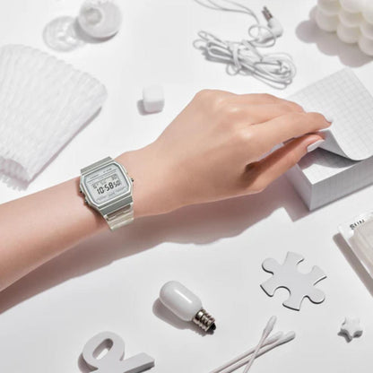 Hand wearing a silver watch on a white surface with minimal objects