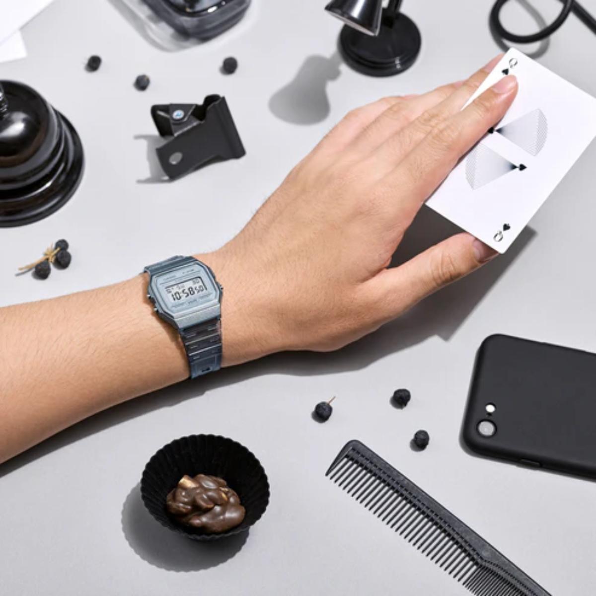 Hand with a watch on a table with various items including a phone, comb, and small bowl.