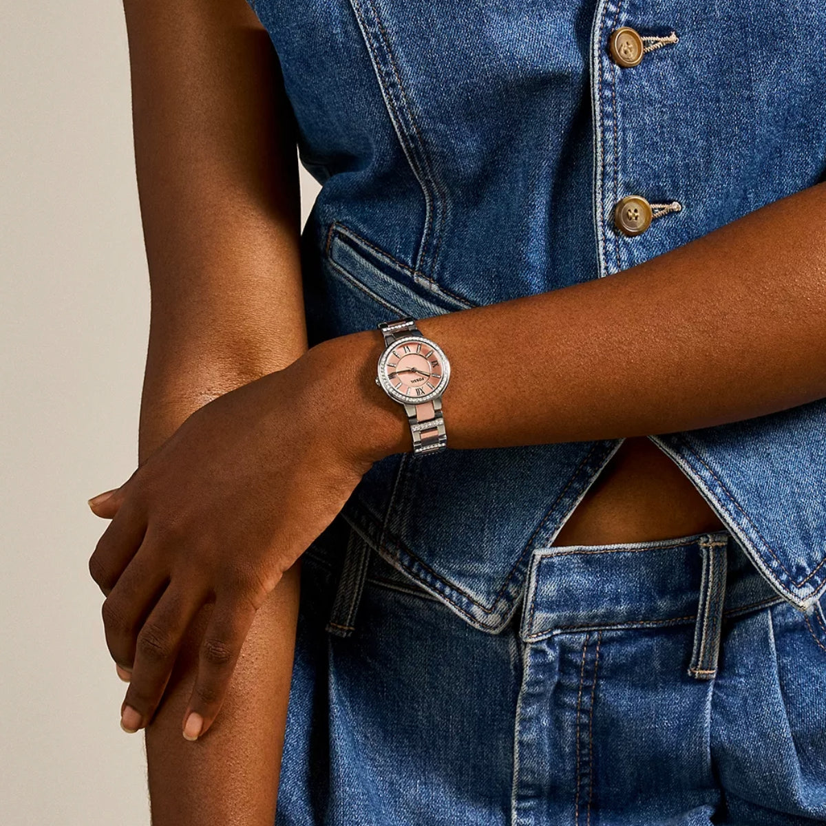 Person wearing a watch with a denim outfit on a neutral background