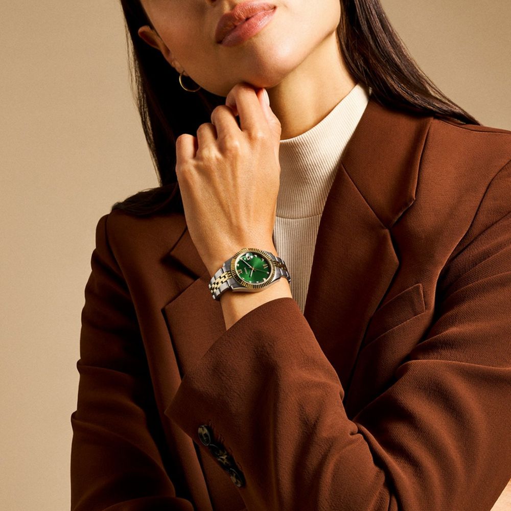 Person wearing a brown coat and green watch on a beige background