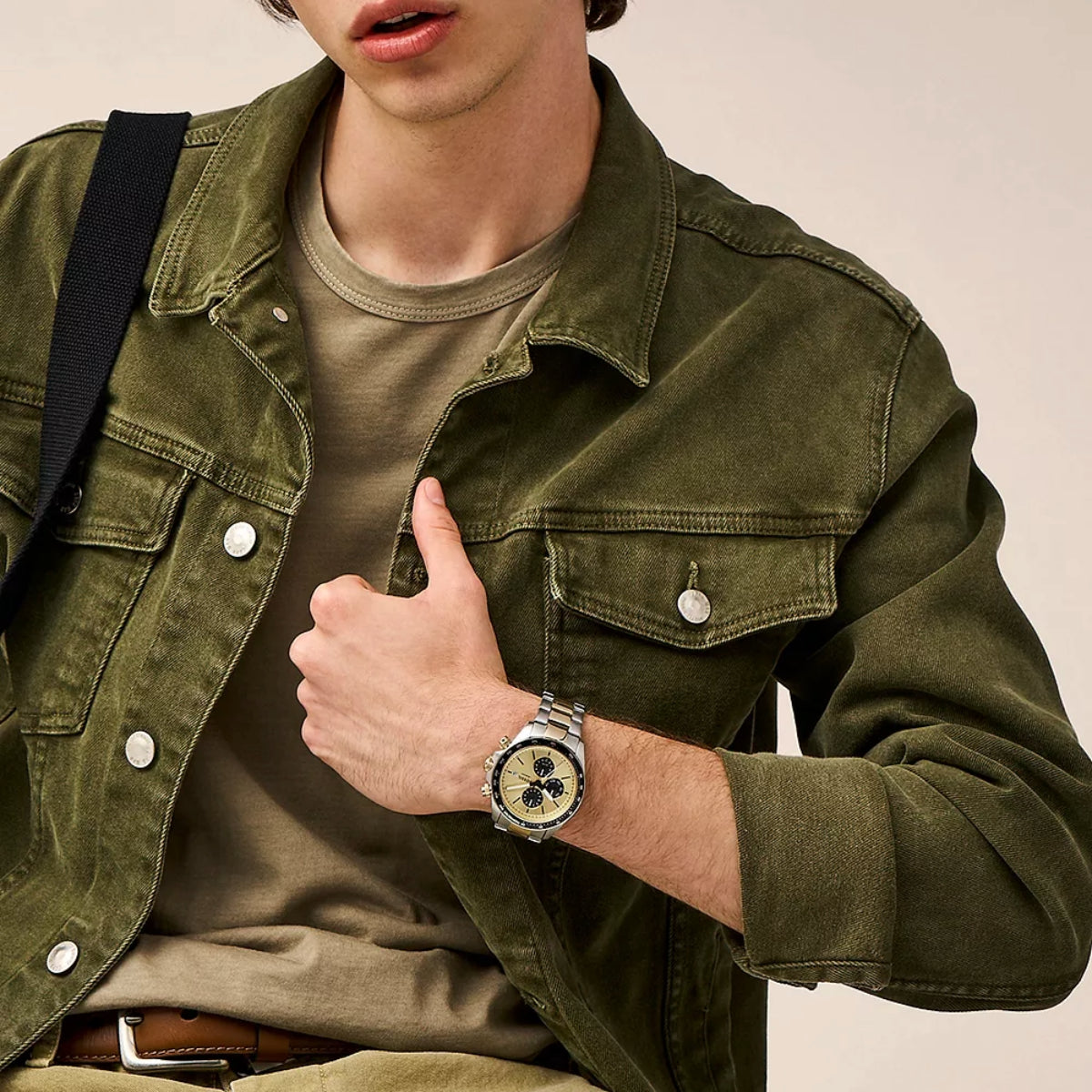 Person wearing a green jacket and a watch, with a neutral background