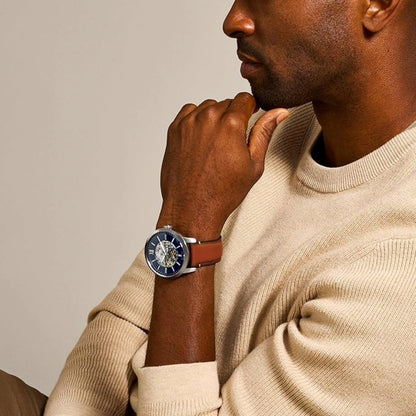 Man wearing a beige sweater and a watch with a brown strap on a neutral background