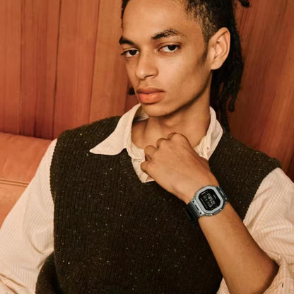 Person wearing a smartwatch with a brown sweater vest and white shirt against a wooden background