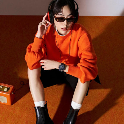 Person wearing an orange sweater and black boots sitting on a red couch with a vintage radio and headphones.
