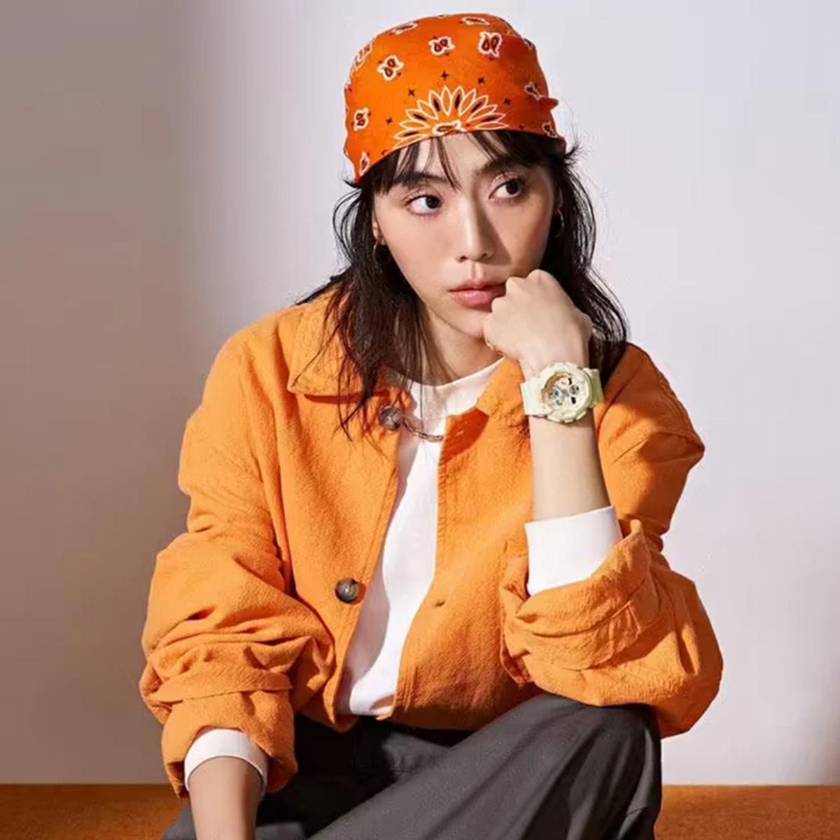 Person wearing an orange jacket and headband, sitting against a plain background