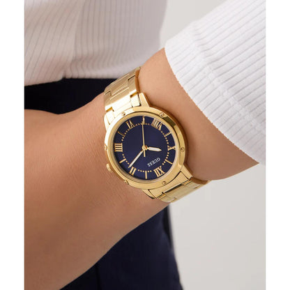 Gold watch with a blue dial on a wrist against a neutral background