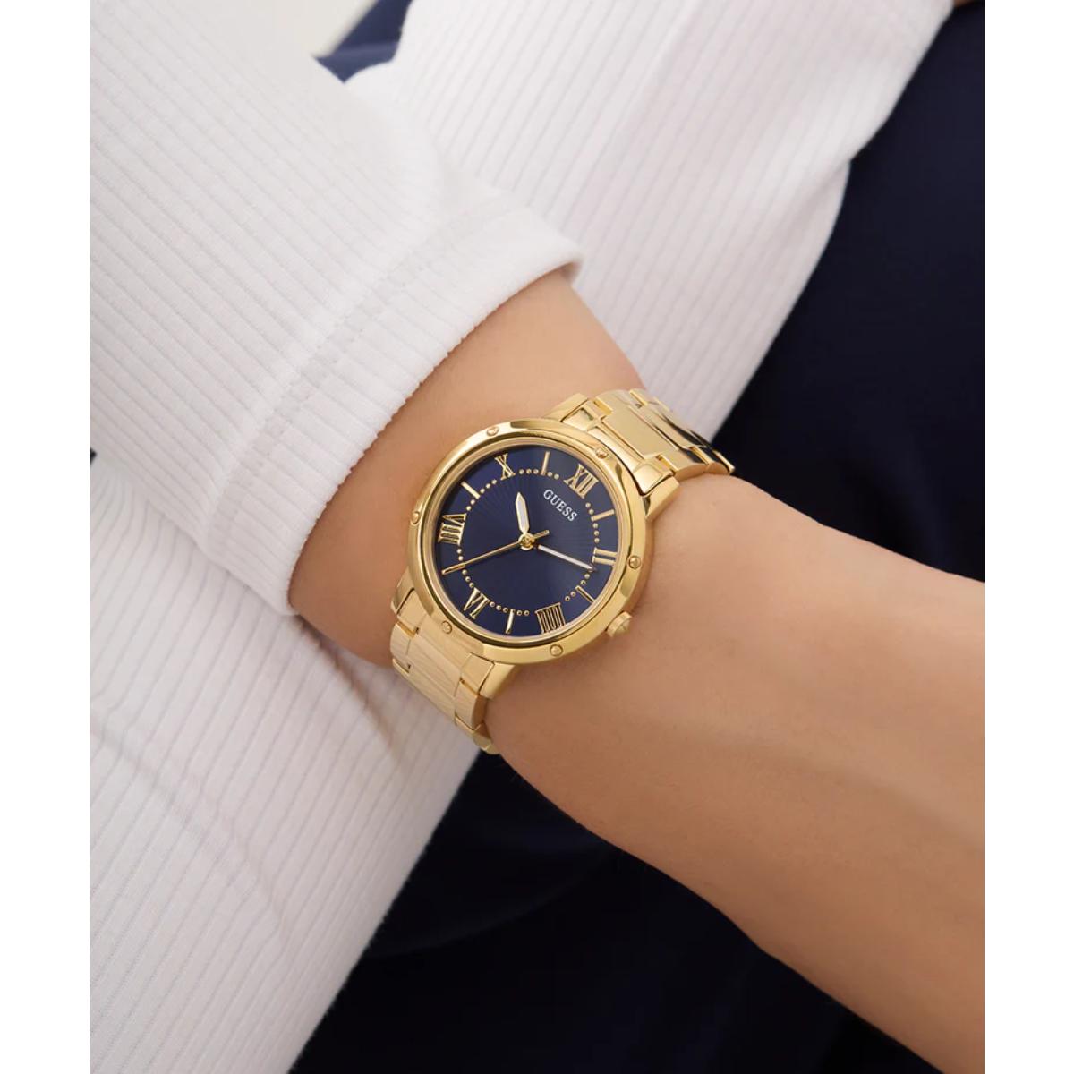 Gold wristwatch with a blue dial on a person's wrist, wearing a white shirt.
