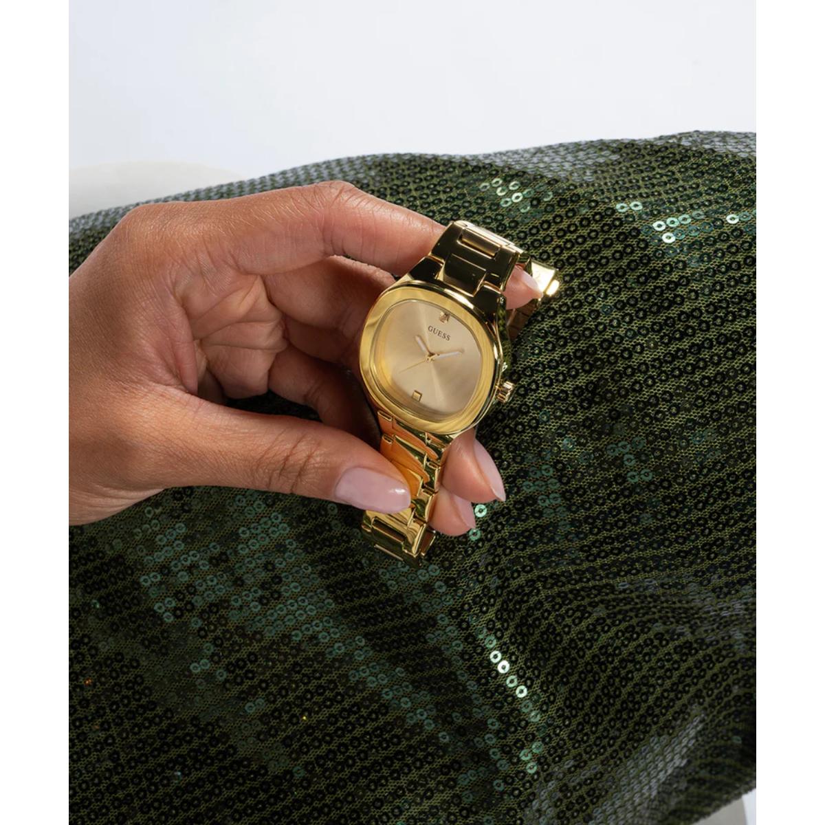 Gold watch held by a hand with a green sequined fabric background