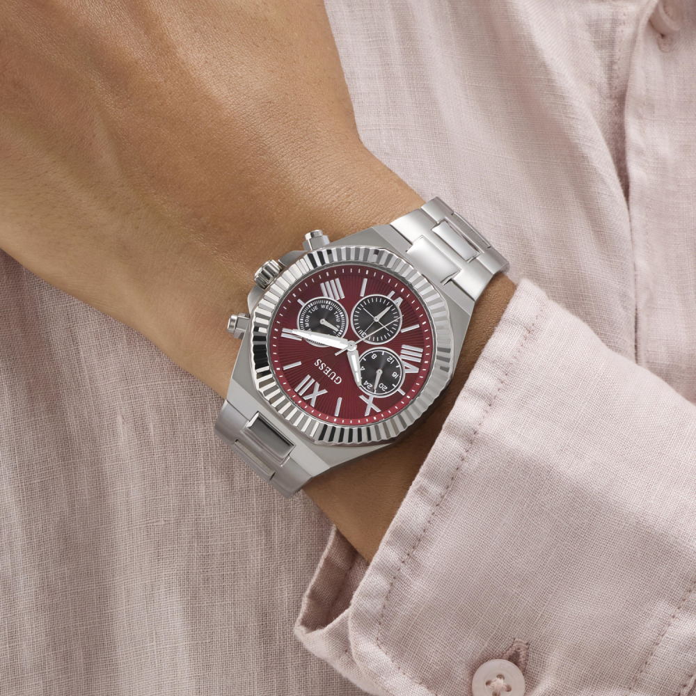Silver watch with a red face on a wrist, wearing a light pink shirt.