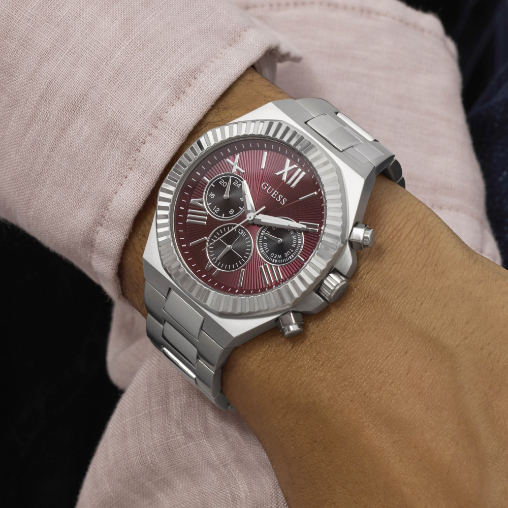 Silver watch with a red face on a wrist, worn by a person in a light pink shirt.