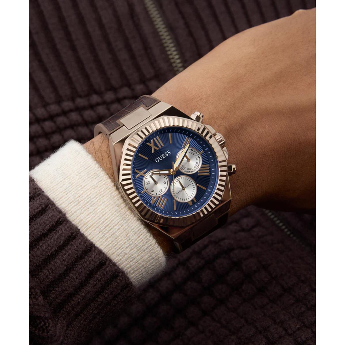 Wrist wearing a rose gold watch with a blue face on a dark background