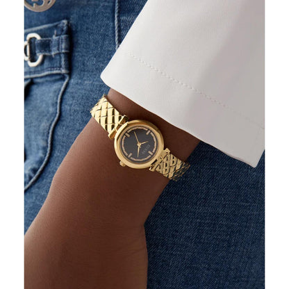Gold watch on a wrist with a white shirt and blue jeans in the background