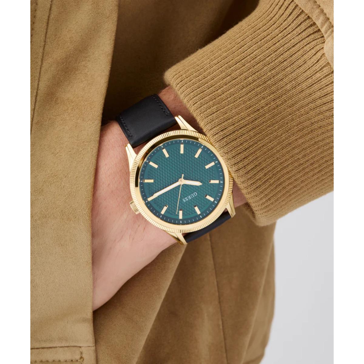 Hand wearing a gold watch with a blue face, against a beige jacket background