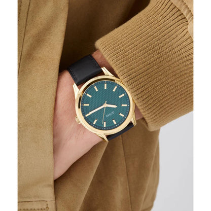 Hand wearing a gold watch with a blue face, against a beige jacket background