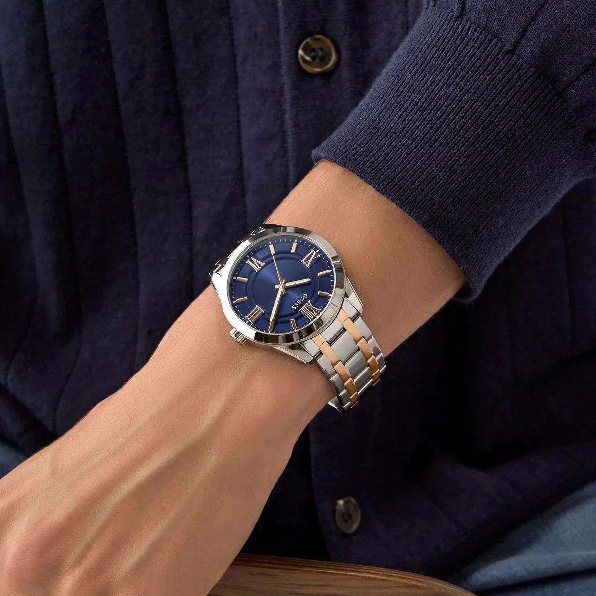 Wrist wearing a watch with a blue face and silver and rose gold band, against a dark background.