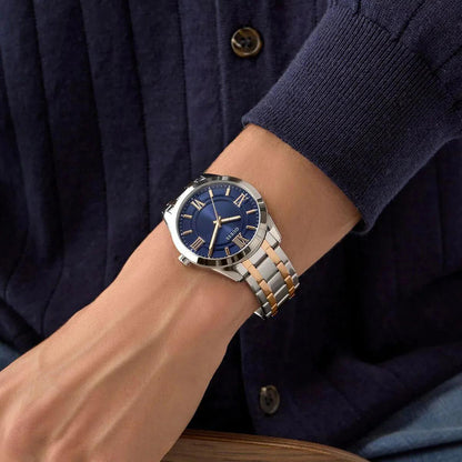 Wrist wearing a watch with a blue face and silver and rose gold band, against a dark background.