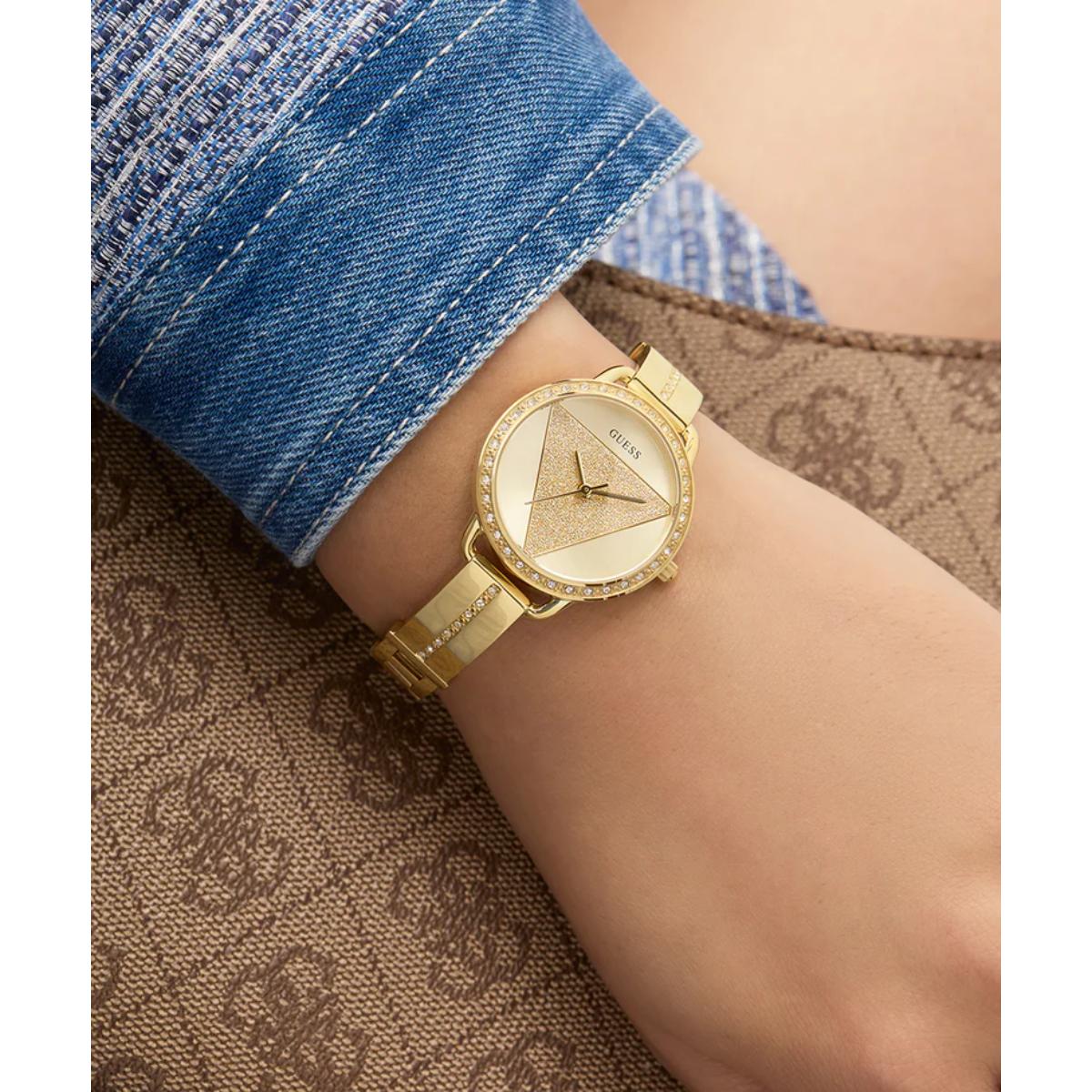 Gold watch on a wrist with denim cuff against a patterned fabric background
