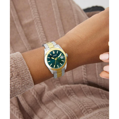 Wrist wearing a silver and gold watch with a green face on a brown textured background