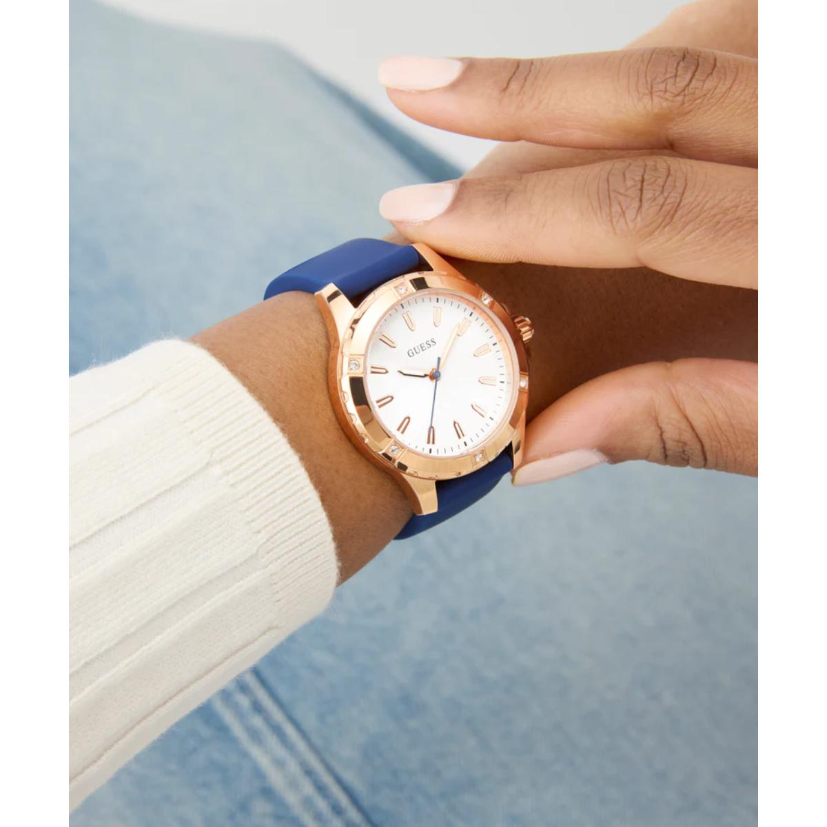 Rose gold watch with blue strap on a wrist against a light blue background