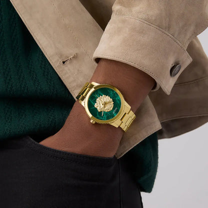 Gold watch with green face on wrist wearing a beige jacket