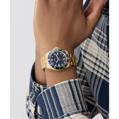 Gold watch with a blue face on a wrist, wearing a plaid shirt.