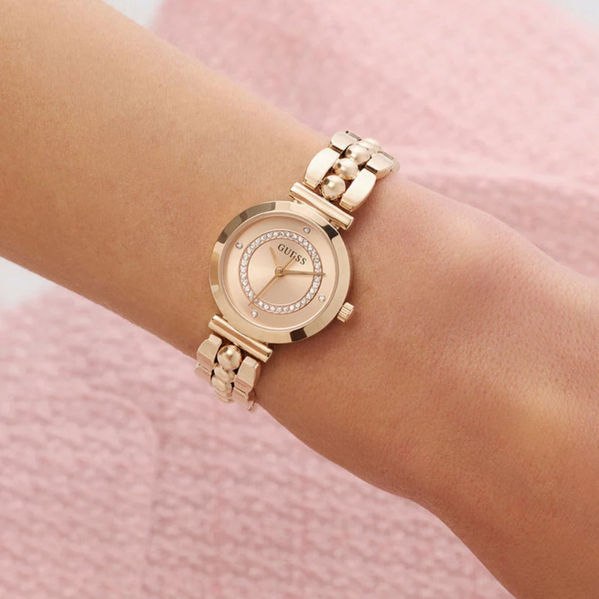 Rose gold watch on a wrist with a pink background
