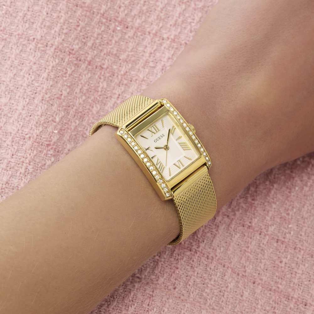 Gold wristwatch with mesh band on a wrist against a pink textured background