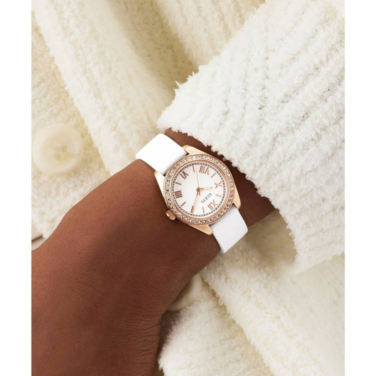 Rose gold watch with white strap on a wrist against a white background