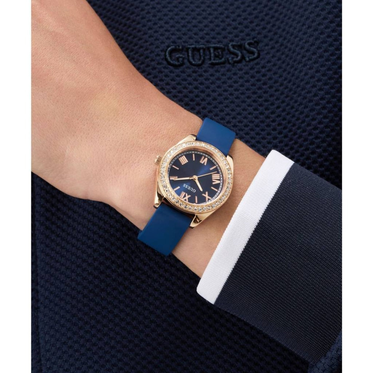 Person wearing a Guess watch with a blue strap on a dark textured background